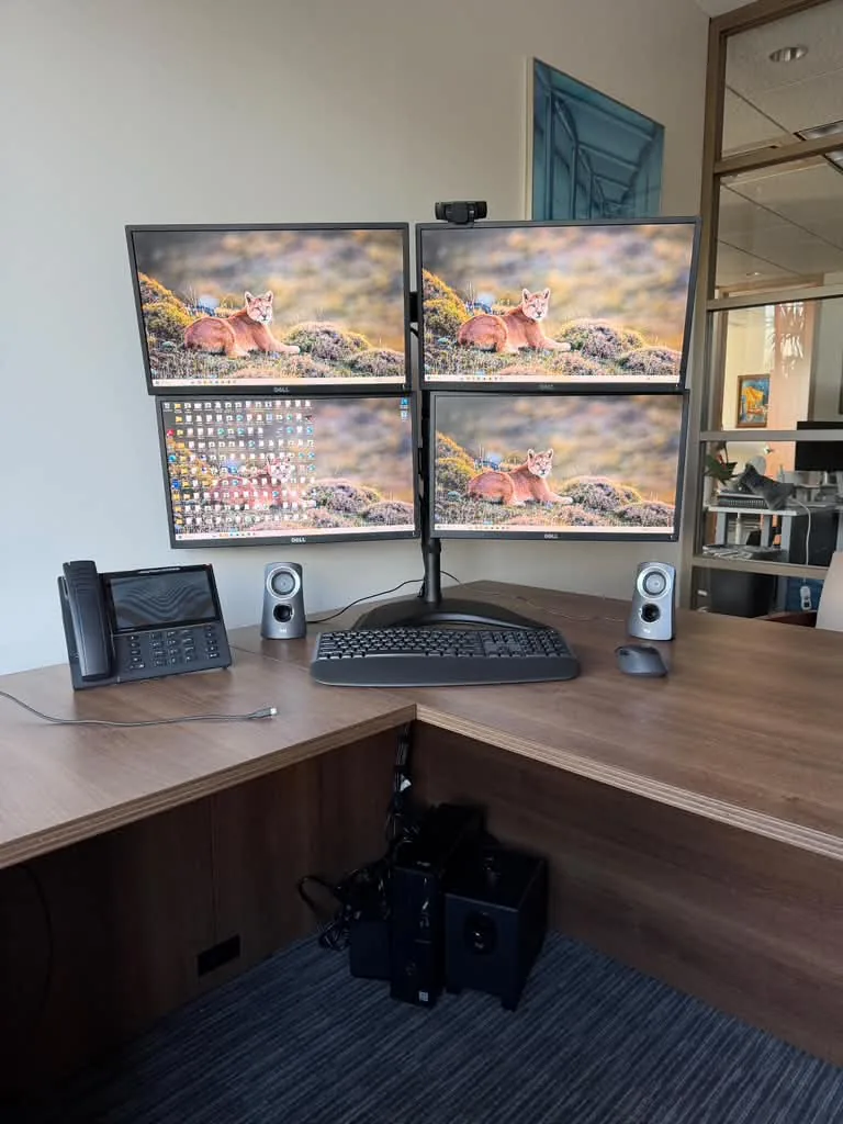 Four monitors on one stand at an office corner desk, installed by FTL Technology Group